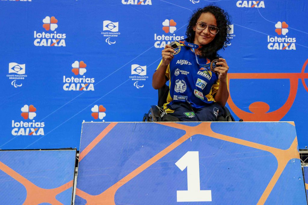 A atleta Lara posa com suas medalhas no primeiro lugar do pódio do Circuito Loterias Caixa 2019. Fim da descrição.
