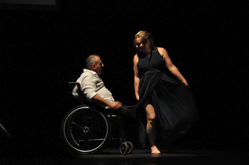 Fernando Passos dança sobre cadeira de rodas ao lado de dançarina. Fim da descrição.