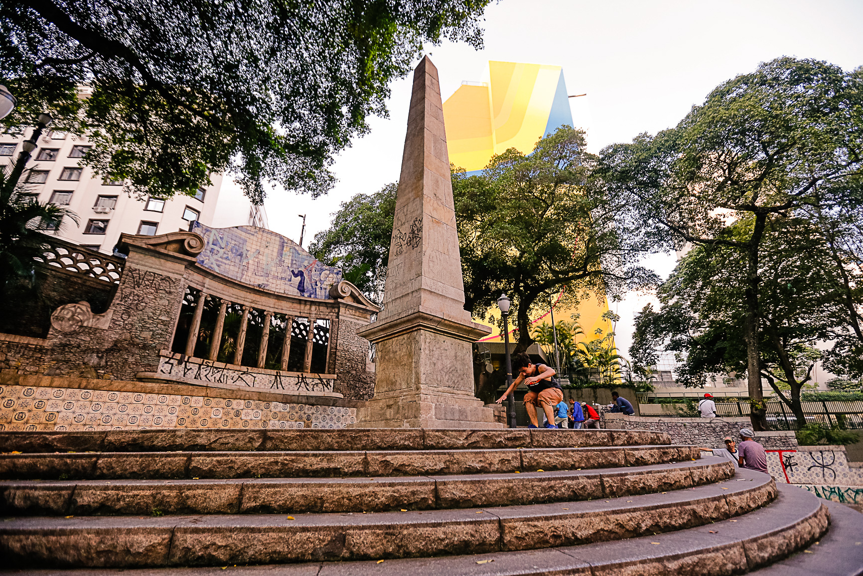 Imagem Largo da Memória, monumento histórico de São Paulo. O monumento é composto por um obelisco no centro de uma base de cinco lances de escada. Fim da descrição.